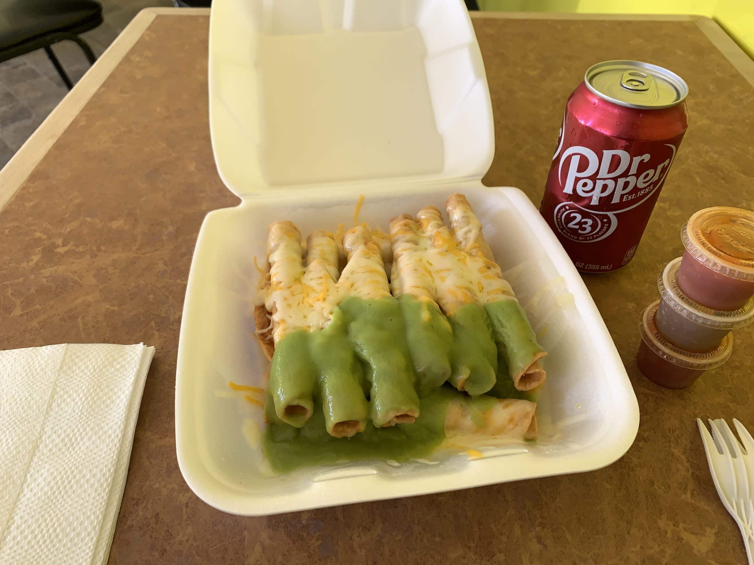Rolled tacos in a white container on a table.