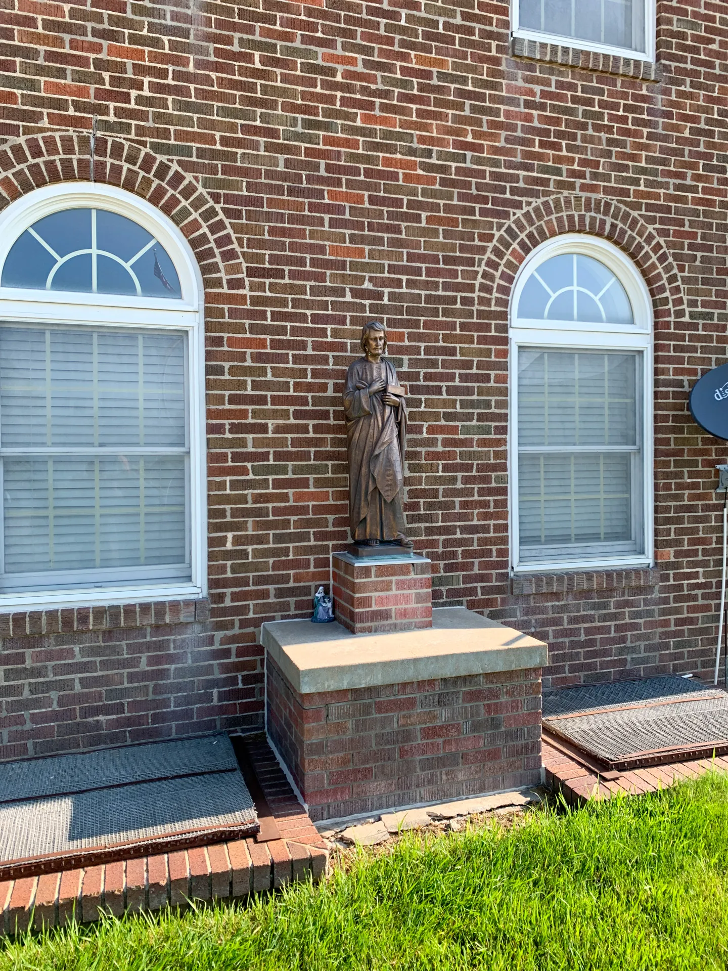 A statue is placed on a brick pedestal between two arched windows on the red brick facade of St Joseph Catholic Church.