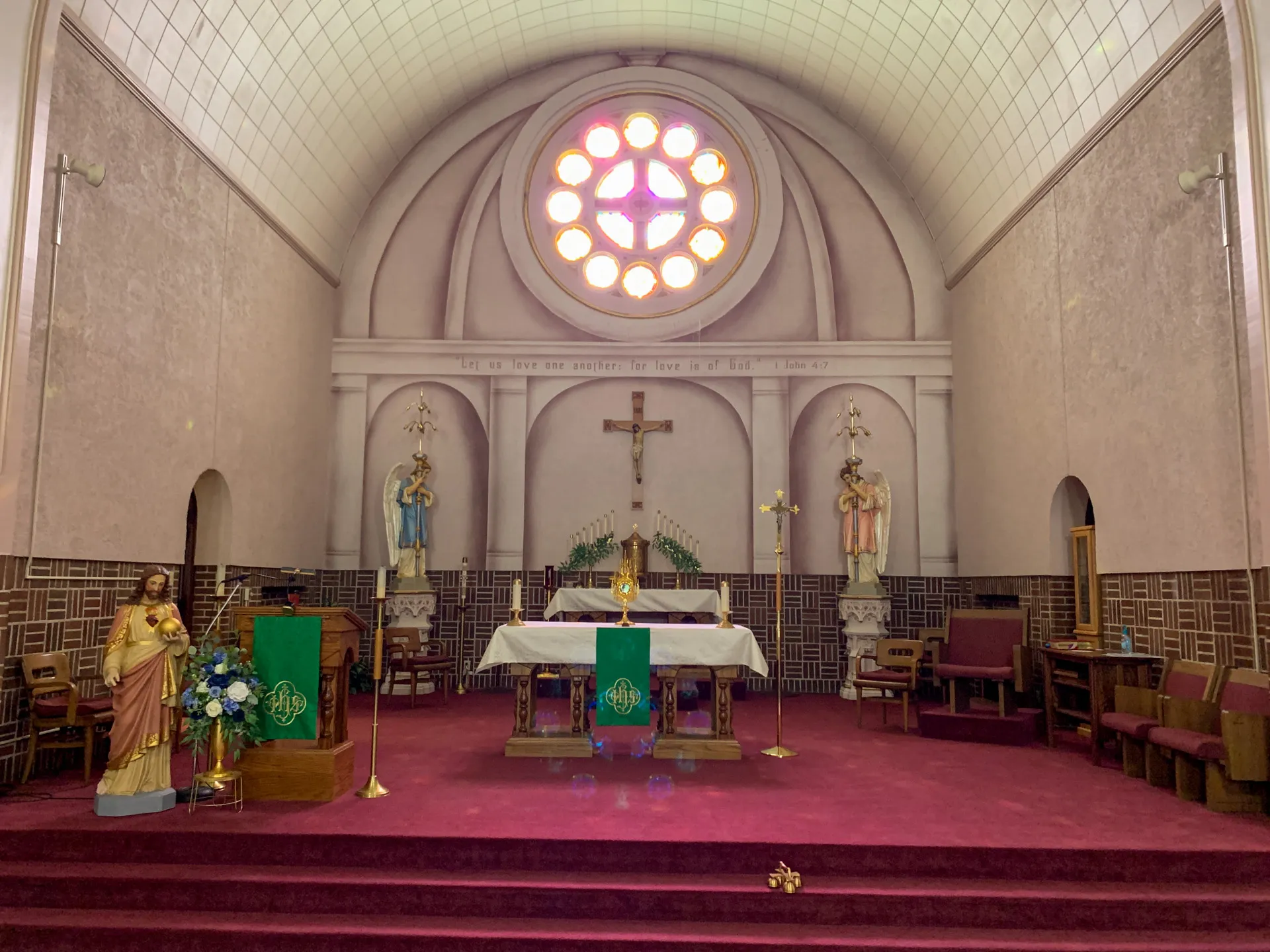 St. Joseph Catholic Church features a sanctuary with a crucifix behind the altar, statues on both sides, and a circular stained glass window above. Red carpet and pews are present. Green liturgical banners adorn the area.
