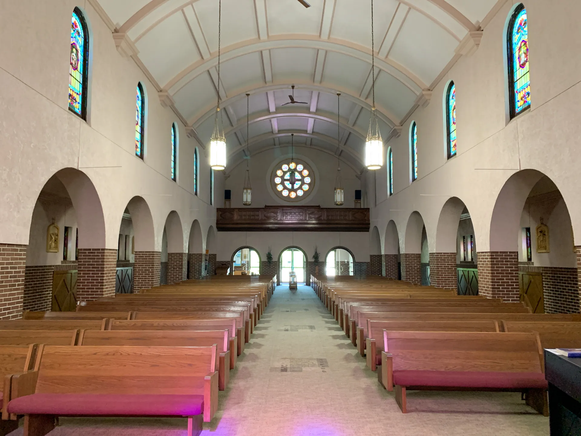 The interior of St Joseph Catholic Church showcases rows of wooden pews, arched ceilings, and stained glass windows, with a backlit entrance in the distance.