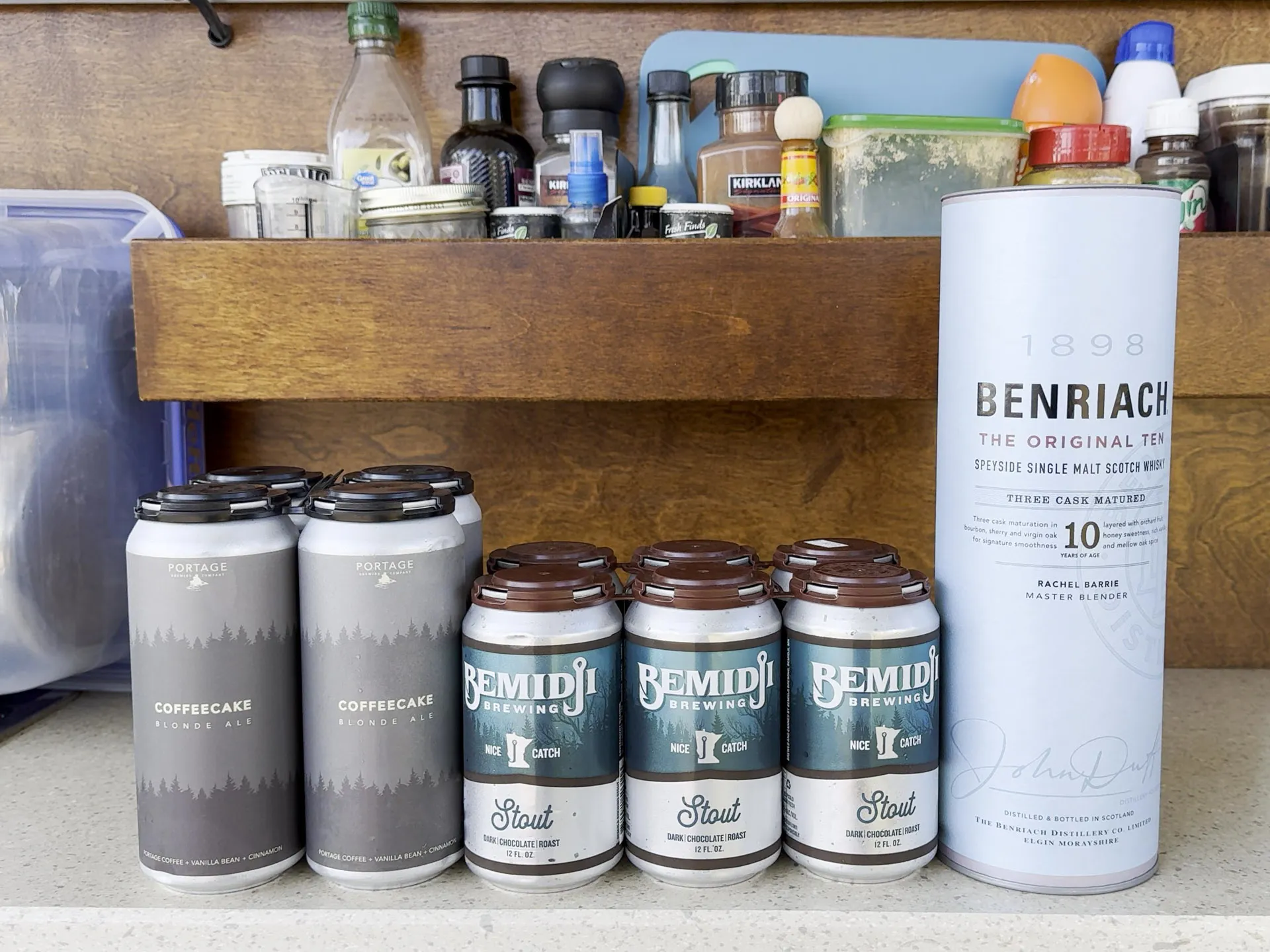 A selection of spirits on a countertop, including four tall cans of Portage Brewing Co. Coffeecake Blonde Ale, four cans of Bemidji Brewing Stout, and a bottle of BenRiach Single Malt Scotch Whisky from Walker Bay.