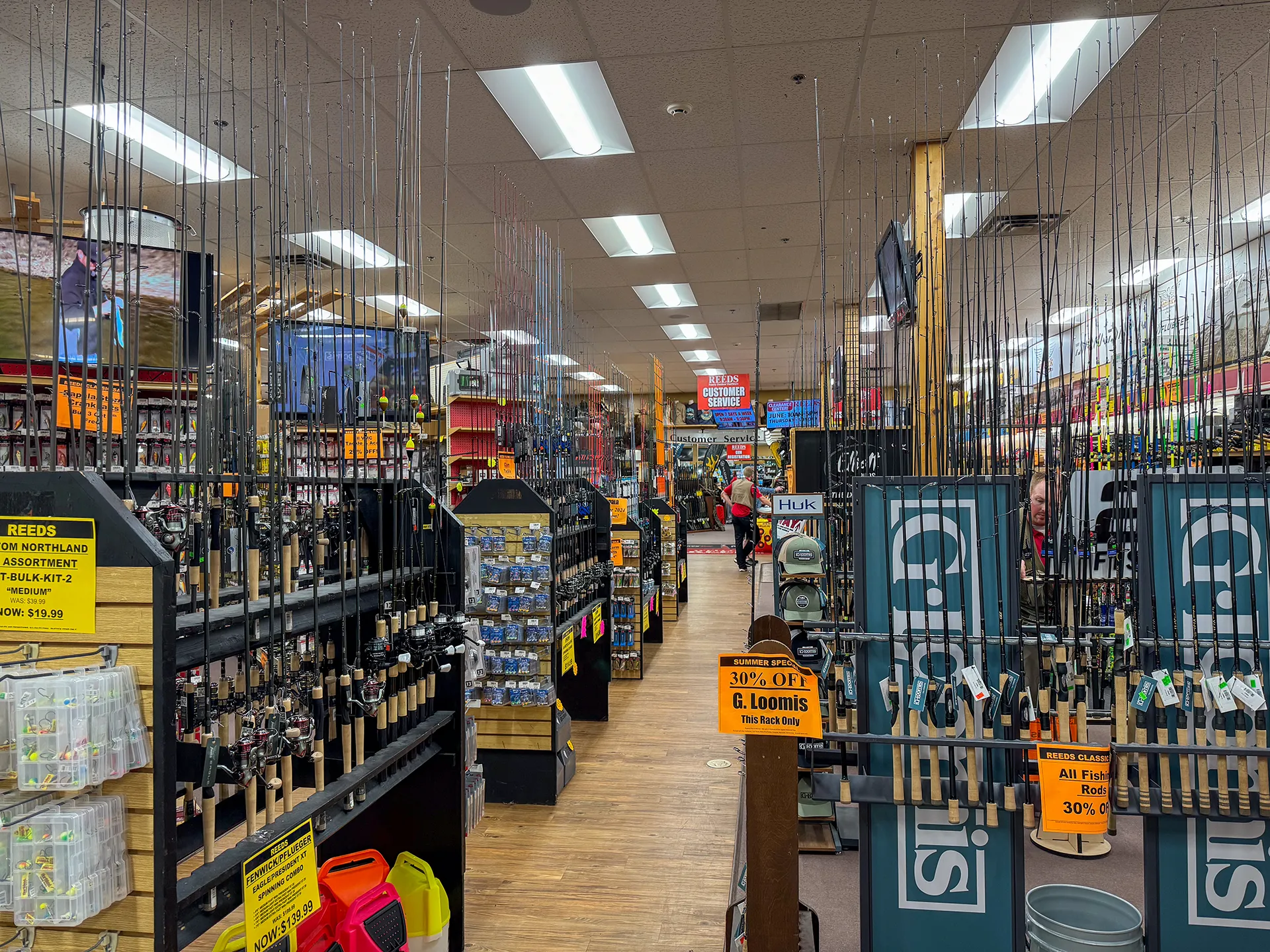 A fishing supply store in Downtown Walker, MN, with aisles of fishing rods, reels, and various gear. Signs advertise a 30% discount on G. Loomis products and select items. The store is well-lit and organized like a lighthouse guiding anglers to their next big catch.