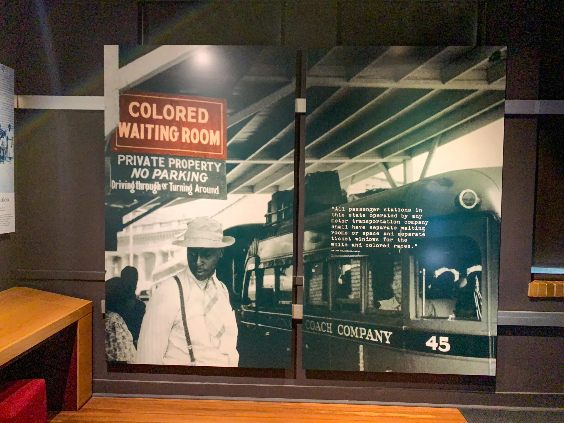 A historical exhibit photo shows a "Colored Waiting Room" sign under a station roof. A man in light clothing and a hat stands nearby. A bus with "Coach Company" and the number 45 is to the right. Text on the bus advises passengers on segregated waiting areas during segregation.