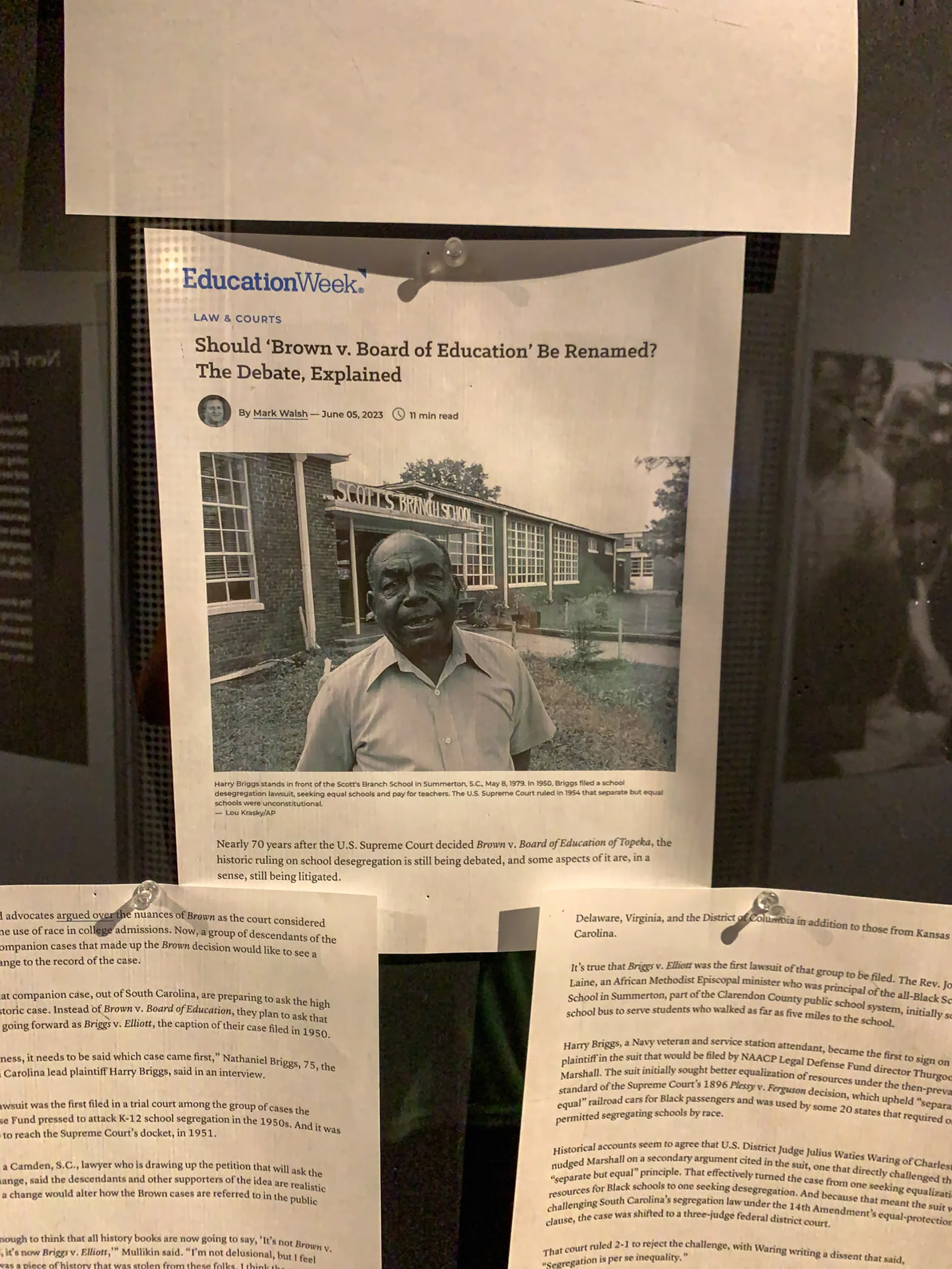 A display features a printed article from Education Week titled "Should 'Brown v. Board of Education' Be Renamed? The Debate, Explained." It includes a large black-and-white photo of a man standing in front of a building. Additional text documents are pinned below.
