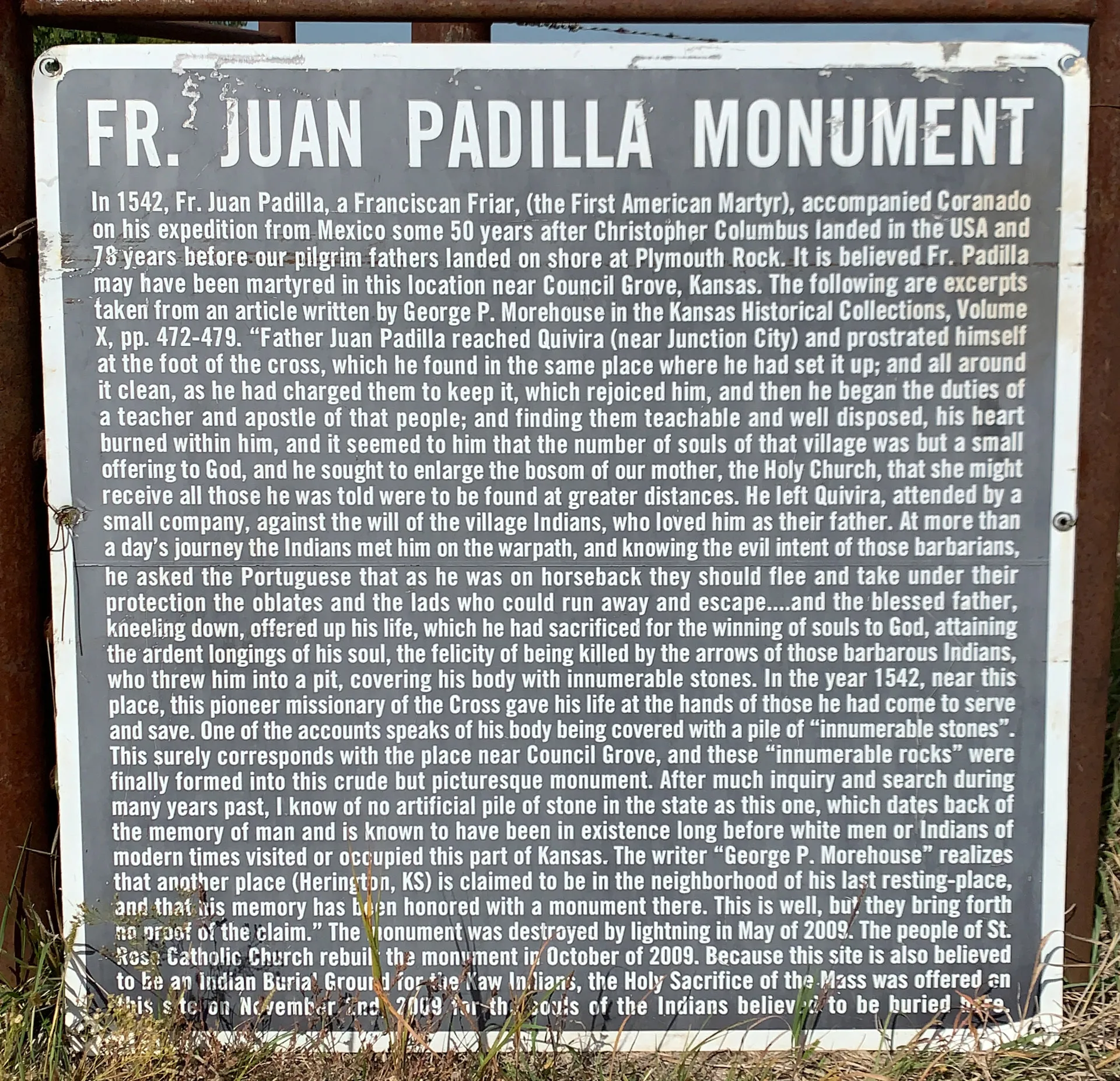 Sign titled "FR JUAN PADILLA MONUMENT" contains dense text about Fr. Juan Padilla, a Franciscan friar and missionary murdered around 1542 in Kansas. Mentions his martyrdom, dedication, and ultimate death, attributed to local Indigenous people. The text is weathered but legible.