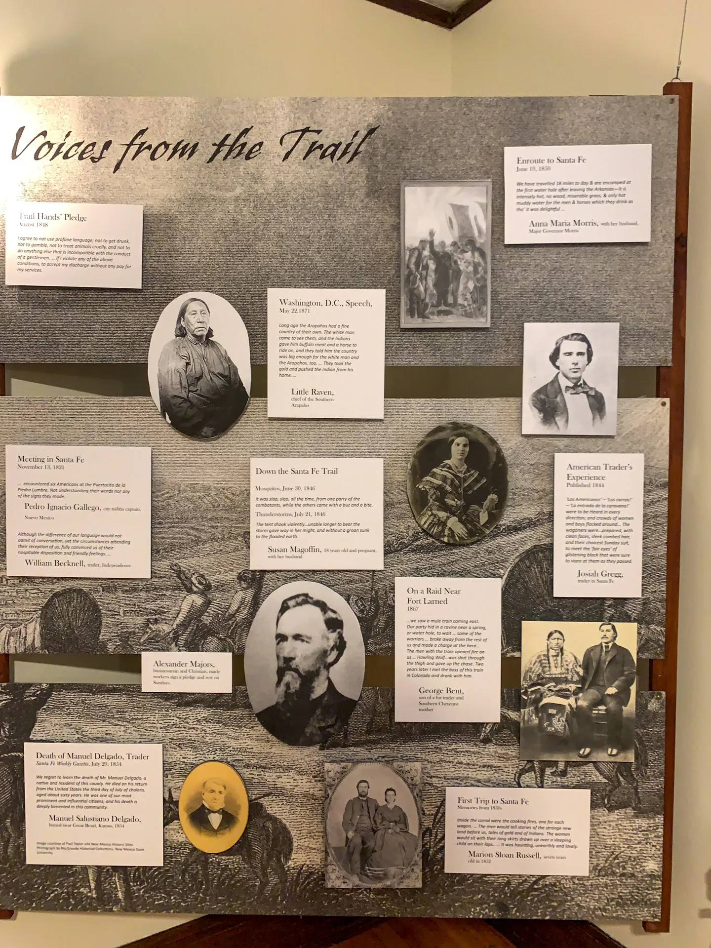 A display titled "Voices from the Trail" features portraits and text panels. It includes historical figures with descriptions of their contributions, events, and locations related to Santa Fe. The background has a vintage illustration of a western scene with horse-drawn wagons.
