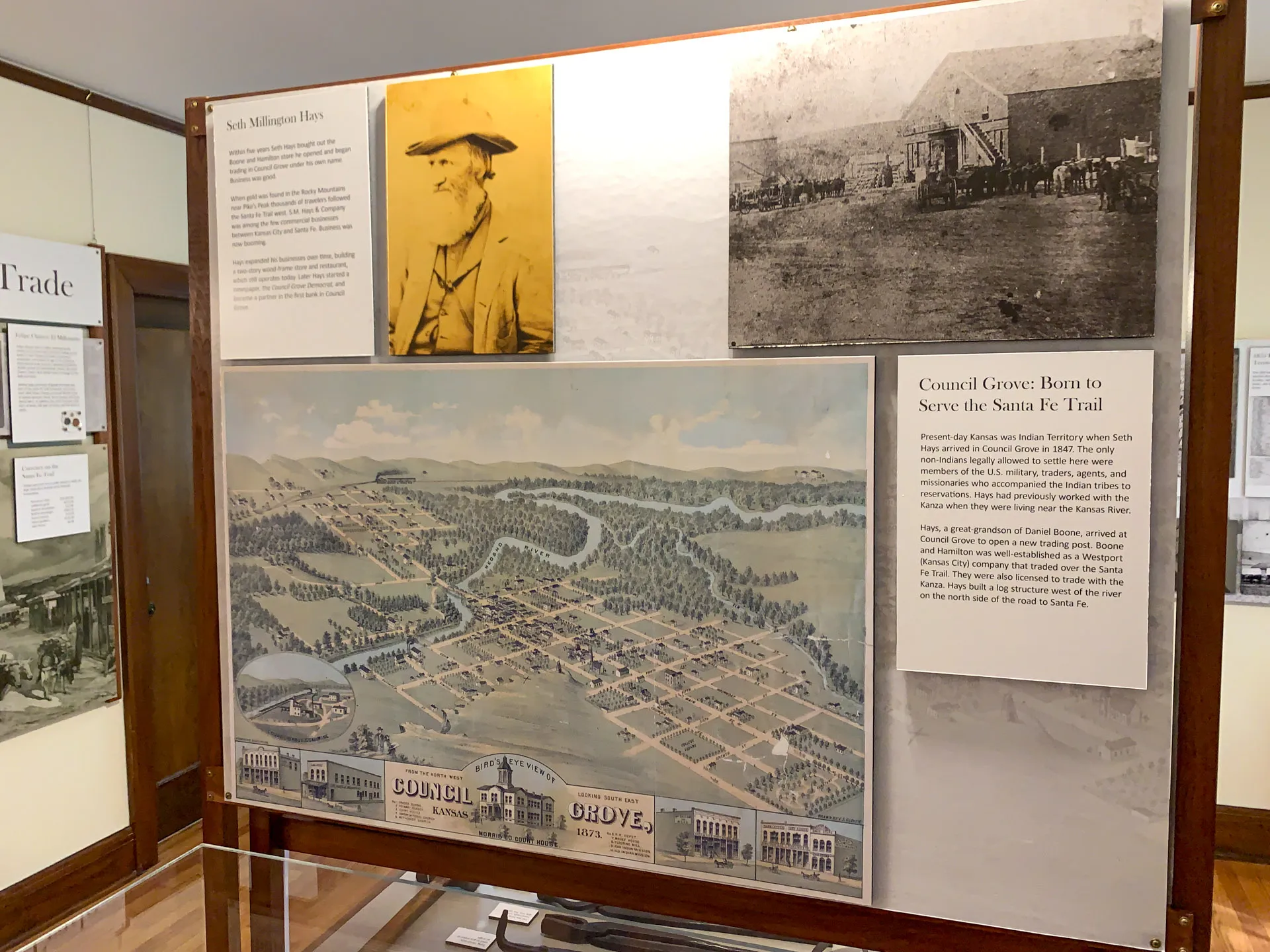 Exhibit display featuring a map of Council Grove, Kansas, with labeled streets and buildings. Includes an old photograph of Seth Millington Hays, a historical description, and a black-and-white photo of settlers and covered wagons. The display is contained within a wooden frame.