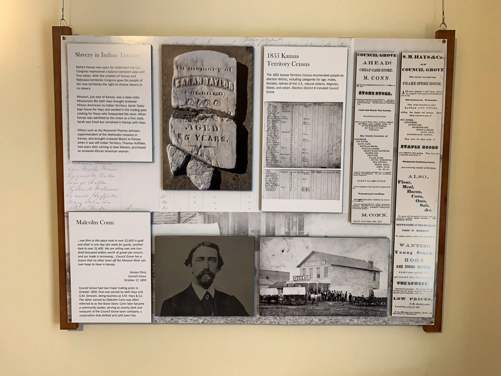 A historical display board features various documents and images. It includes a gravestone photo, text about 1855 Kansas Territory Census, and a section on Malcolm Conn. There's a black-and-white portrait of a man, alongside an old photograph of a wagon and people outside a building.