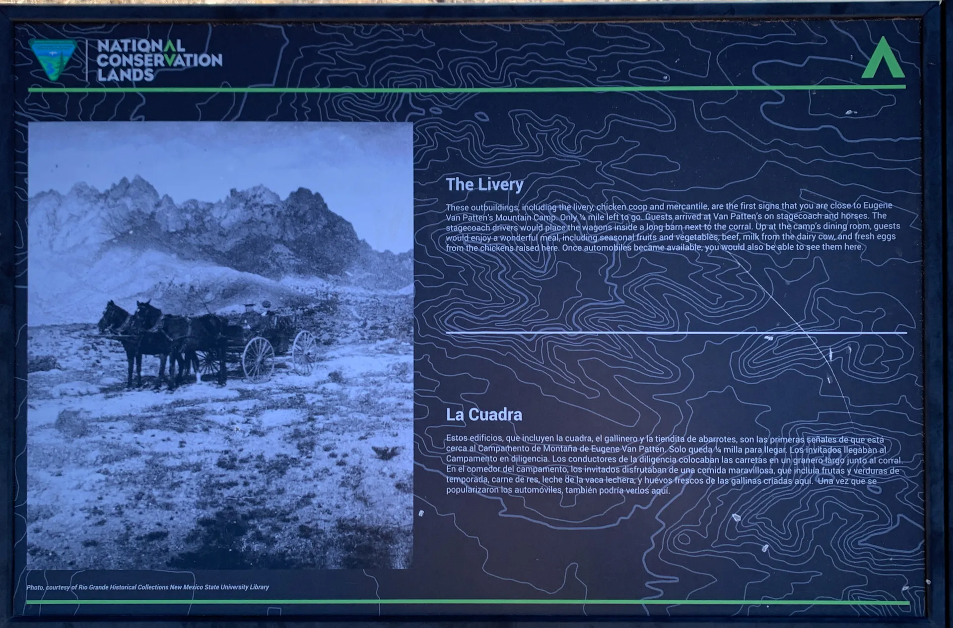 A framed informational display with a black-and-white photo of a horse-drawn wagon in rocky terrain. Text titled "The Livery" in English and "La Cuadra" in Spanish describes historical use of mule teams and wagons. Background features contour lines, with "National Conservation Lands" branding.