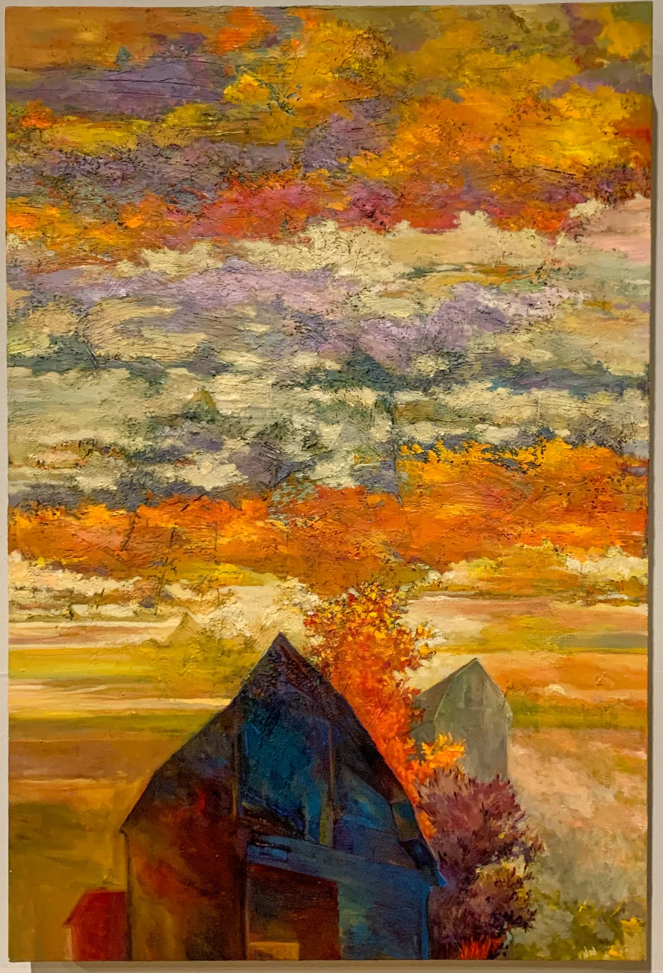 A colorful, textured painting of a rural landscape at sunrise or sunset. Two barn-like buildings are in the foreground, under a vibrant sky with layers of orange, yellow, and purple clouds. Autumnal trees with red and orange leaves add contrast to the scene.