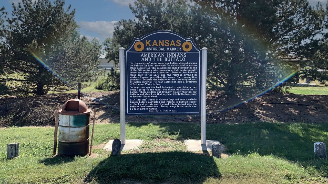 An AMERICAN INDIANS AND THE BUFFALO Historical Marker in front of a tree with a rainbow in the background.